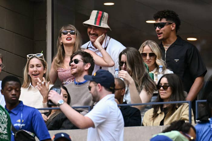 Taylor Swift with a group of friends, including Gigi Hadid, seated together at a tennis match, laughing and enjoying the event