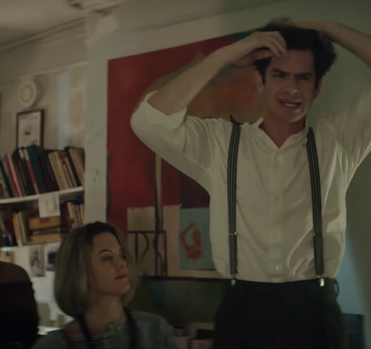 Andrew Garfield stands, raising his hands to his head in a room while singing