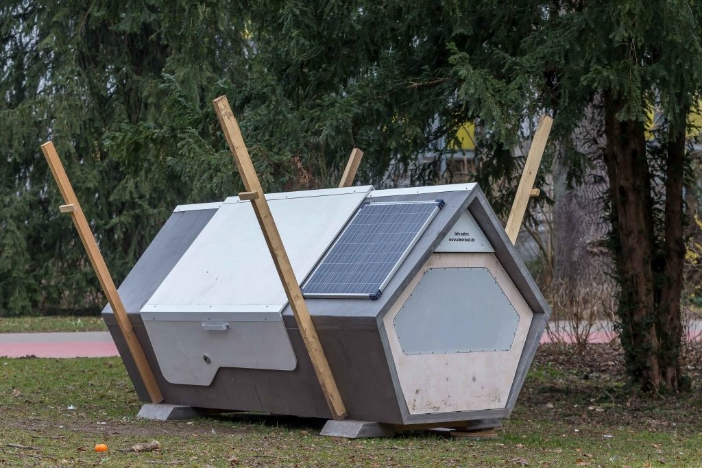 Hexagonal-shaped shelter with solar panels and wooden supports, placed outdoors among trees