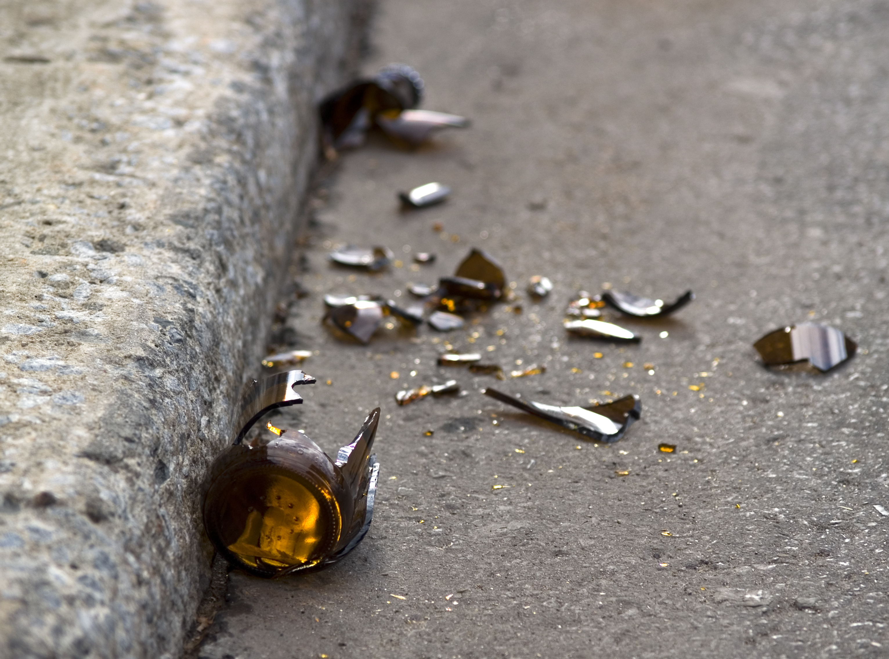 Broken glass bottle pieces scattered on the ground near a curb