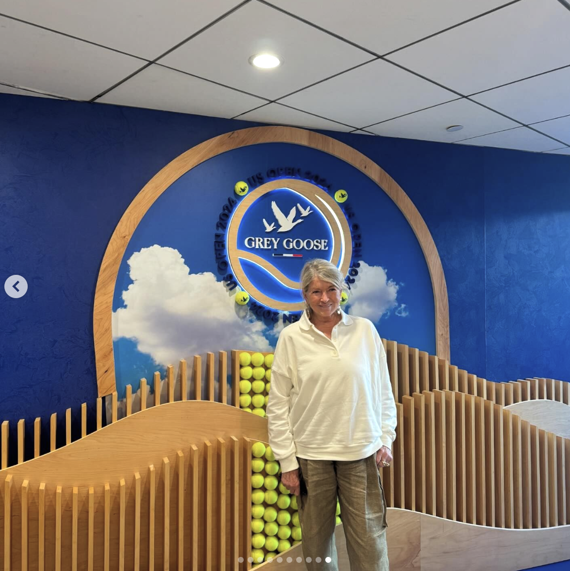 Martha Stewart stands in front of a Grey Goose display decorated with tennis balls and a wooden wave-like structure