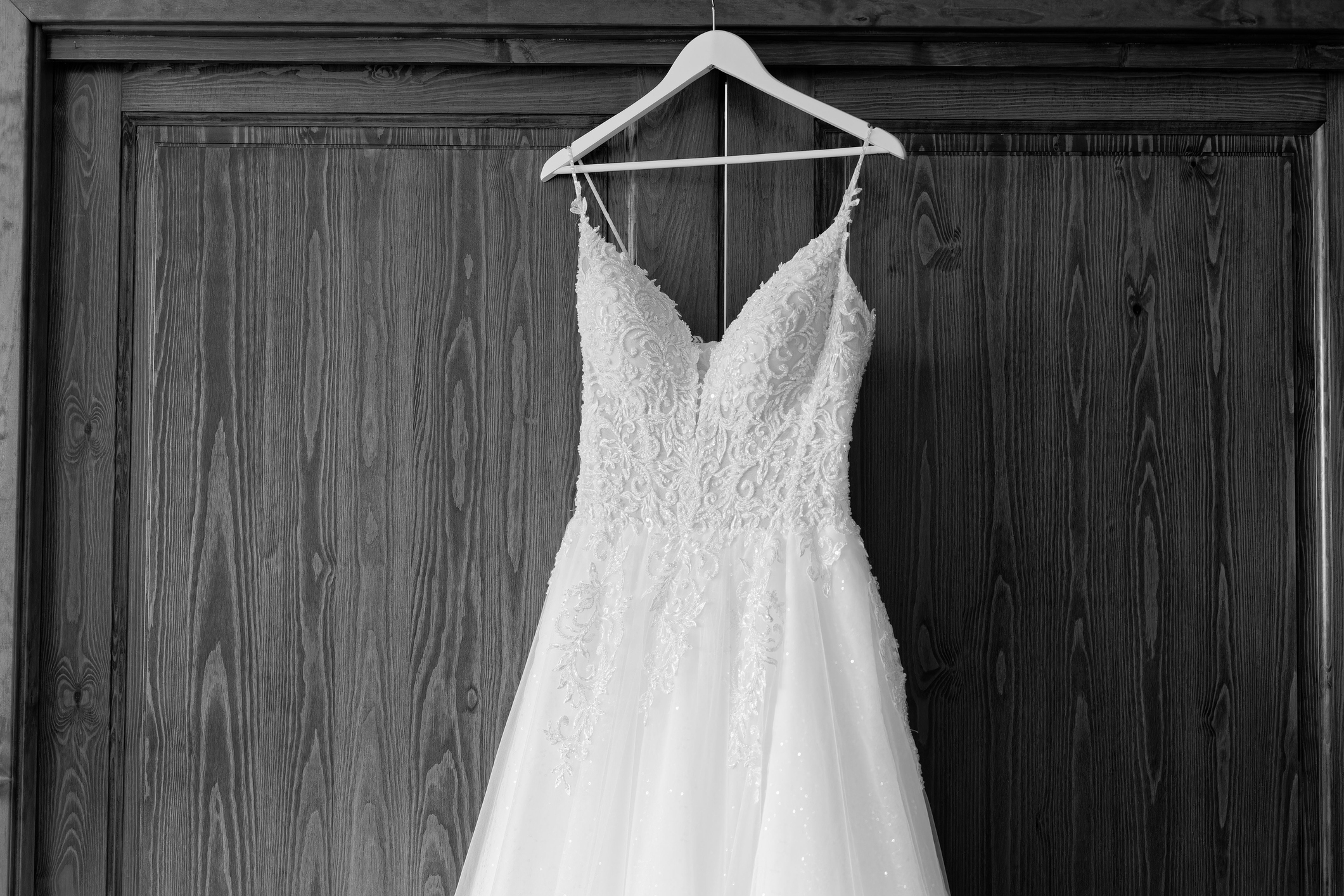 A lace wedding dress with a fitted bodice and flowing skirt is hanging on a wooden door, ready for a wedding ceremony