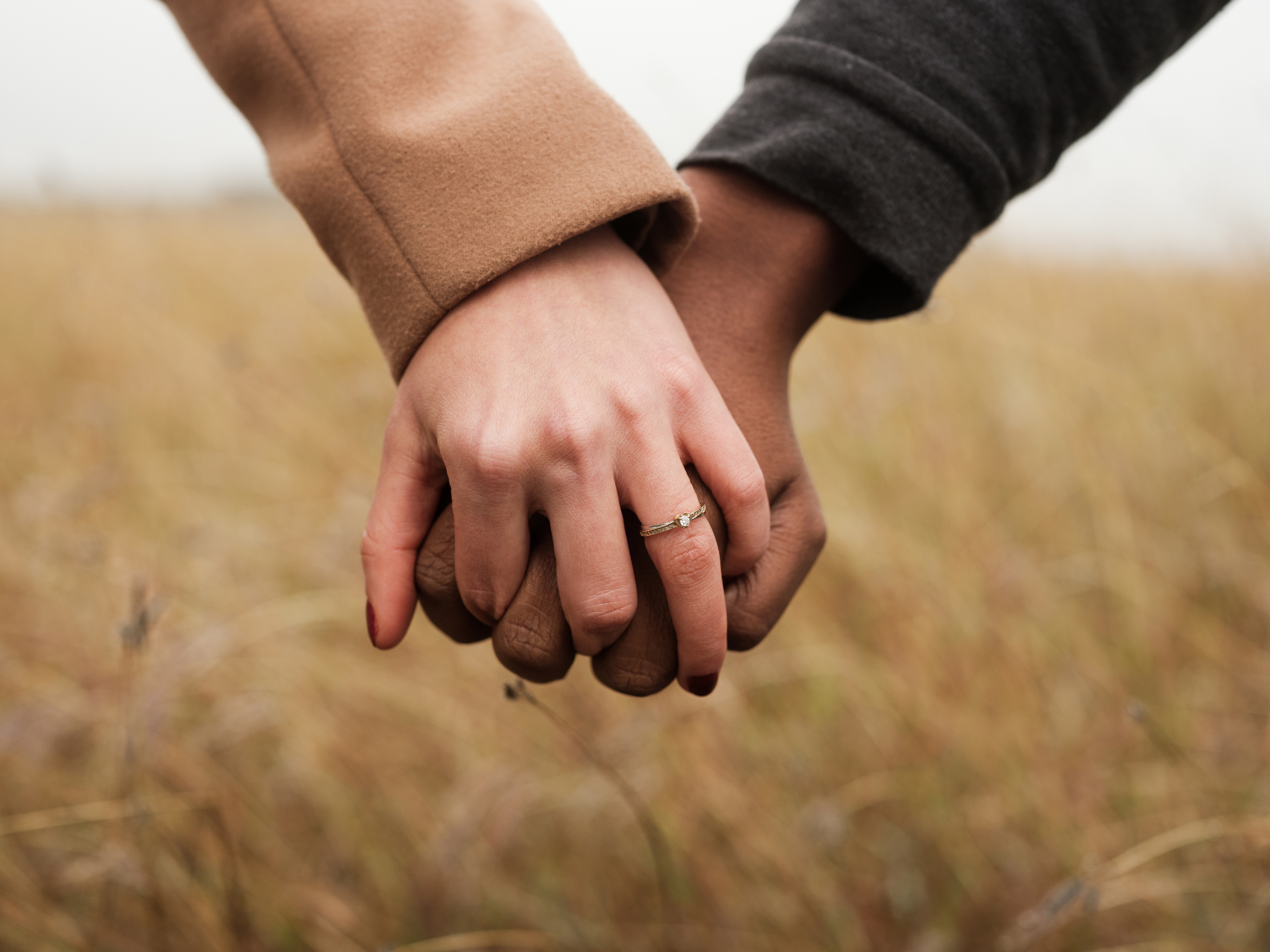 Close-up of two people holding hands, one wearing an engagement ring, symbolizing love and connection