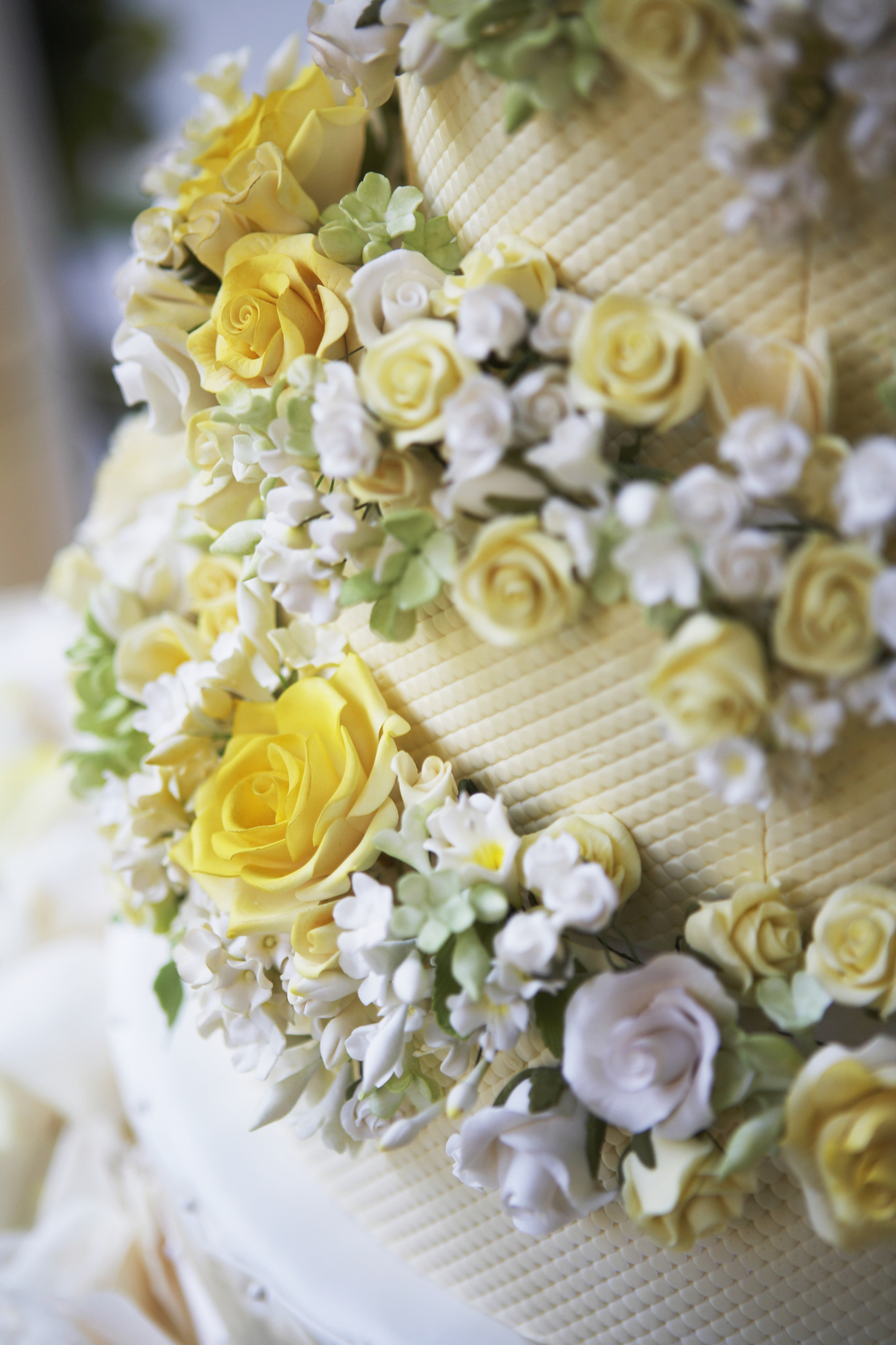 Close-up of a wedding cake decorated with intricate floral designs, featuring yellow and white roses, greenery, and detailed icing work
