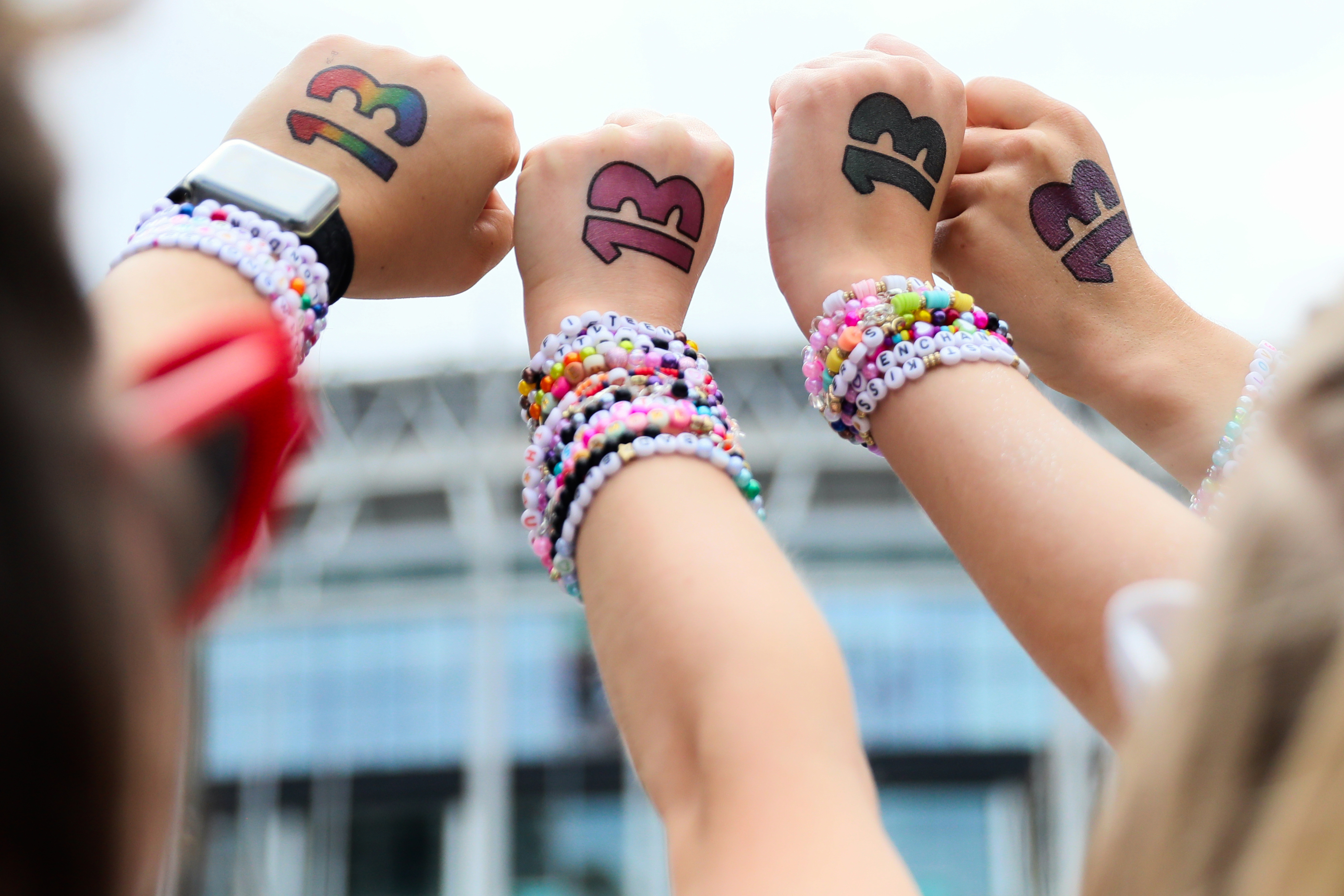 Swifties with the number 13 written on their hands showing off friendship bracelets