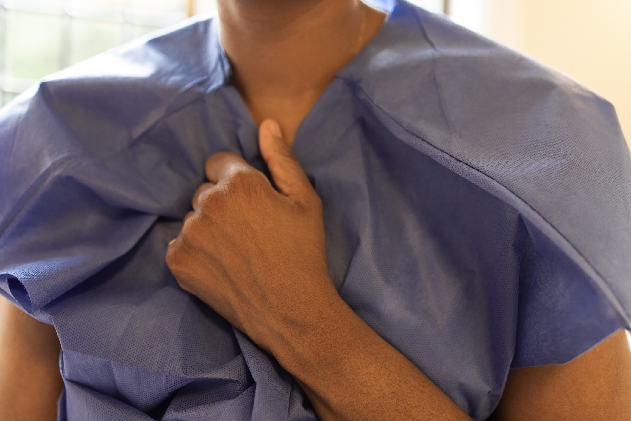 A person wearing a medical gown holds the front of the gown tightly near their chest