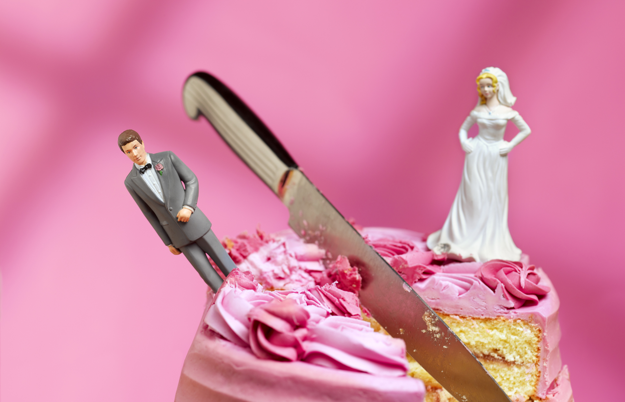 Wedding cake with bride and groom figurines. Bride is in a white dress with a veil. Groom is in a suit. Cake is partially sliced