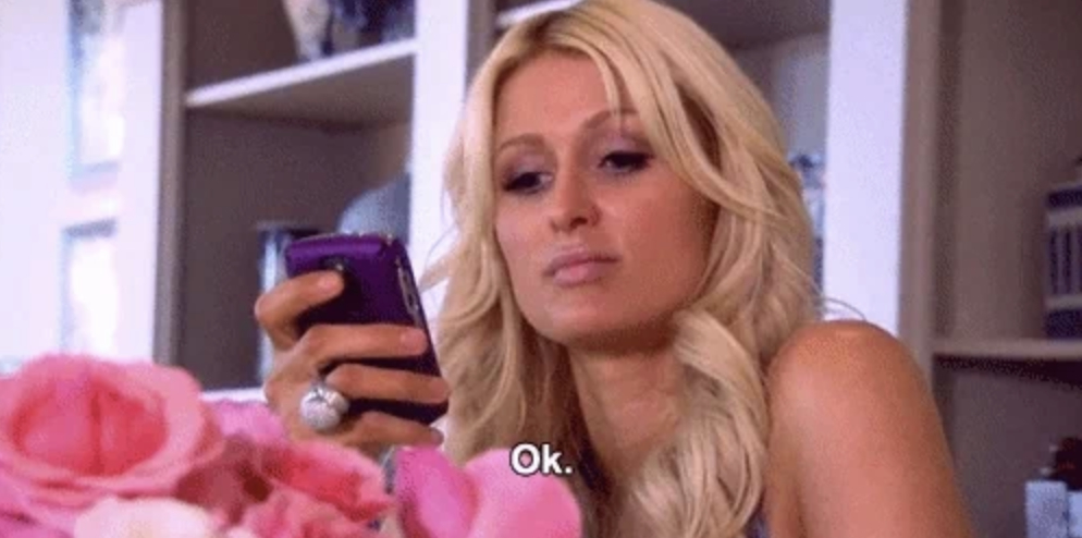 Paris Hilton looks at her phone with a serious expression, while the text "Ok." appears at the bottom. Pink flowers are visible in the foreground