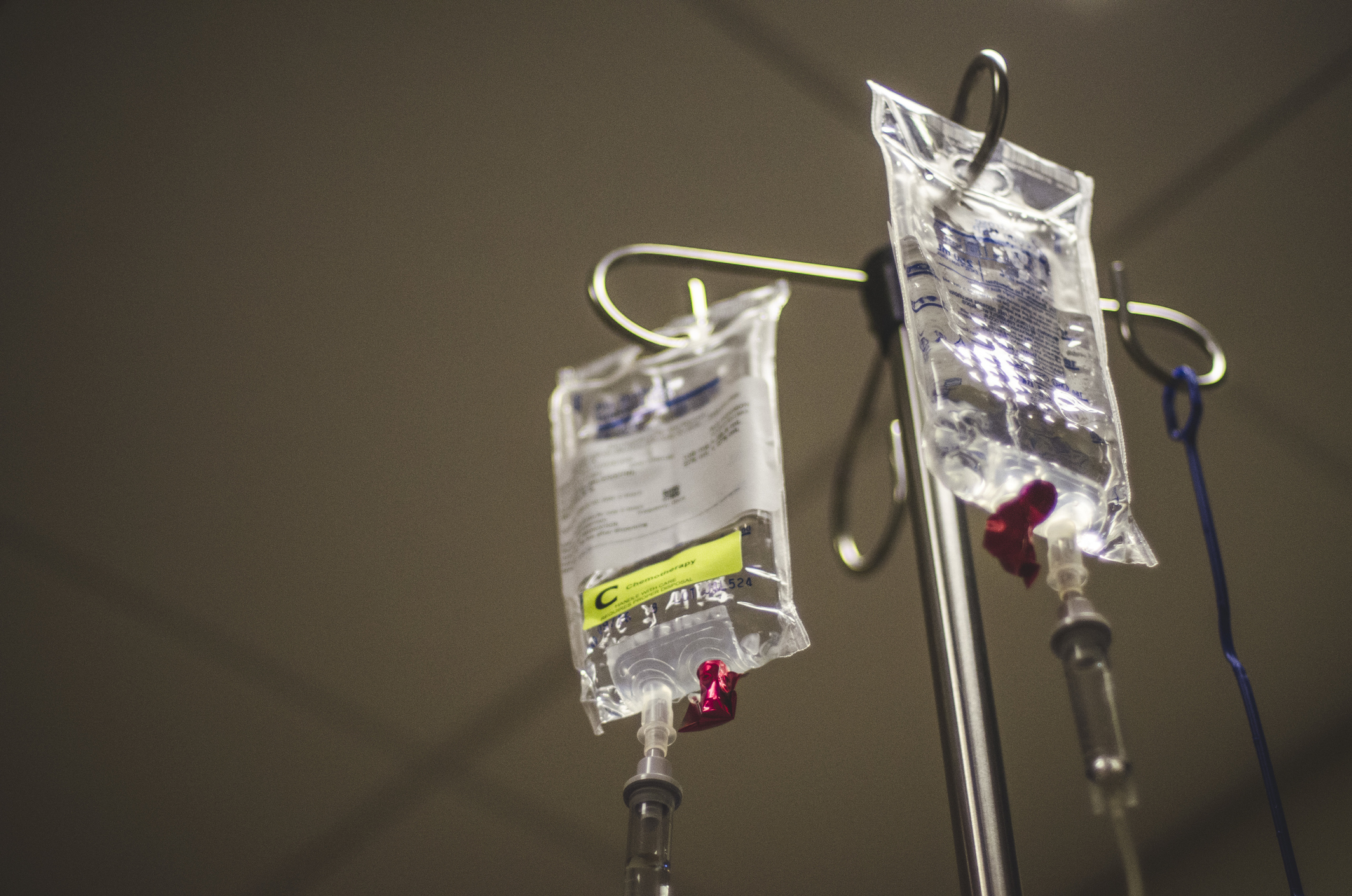 Two IV bags with attached tubes hang from a metal pole, likely used for medical treatment in a hospital setting