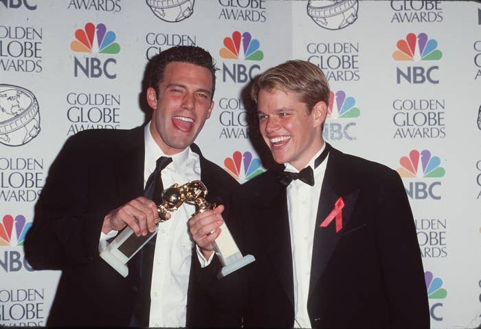 Ben Affleck and Matt Damon celebrate with Golden Globe awards, both dressed in black tuxedos on the red carpet, smiling in front of the Golden Globe Awards backdrop