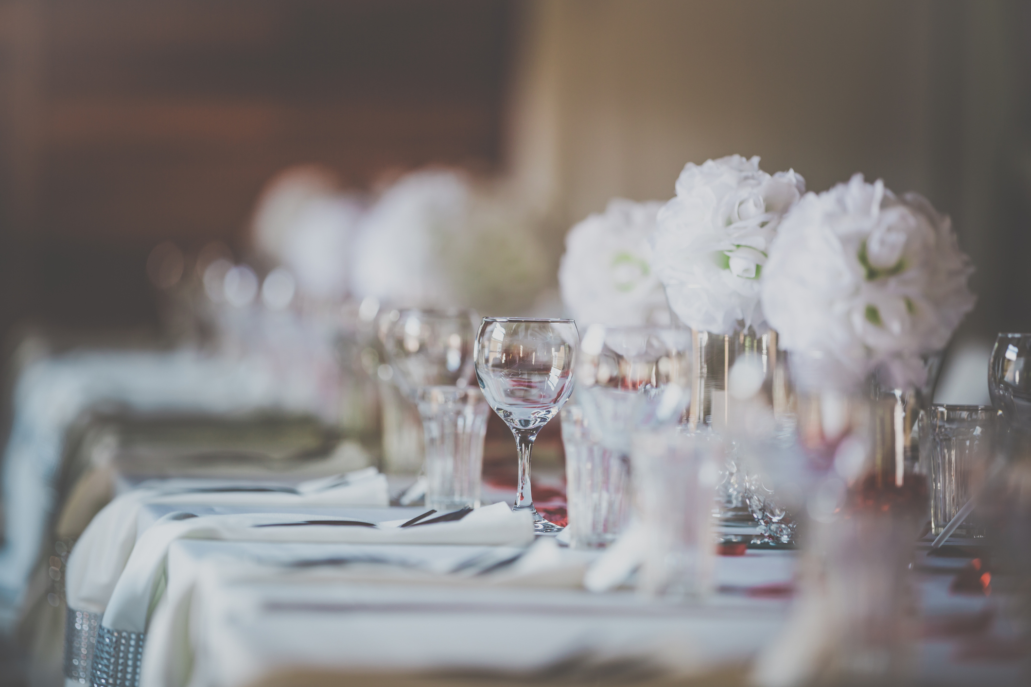 Elegant wedding table setting with white floral centerpieces, crystal glassware, and neatly placed tableware, creating a refined and sophisticated atmosphere