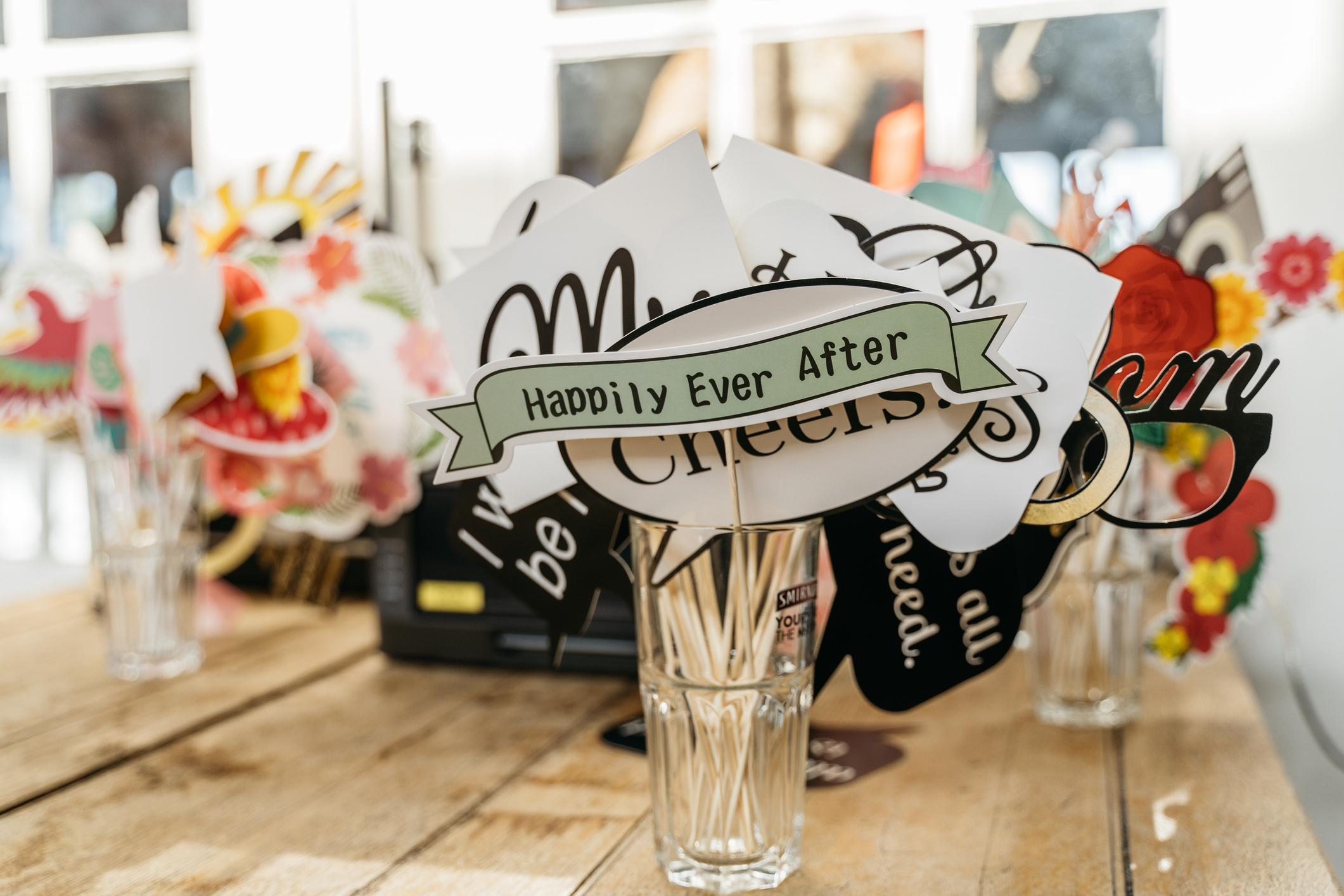 A variety of wedding-themed photo booth props in glasses, with the main sign reading "Happily Ever After" on a wooden table