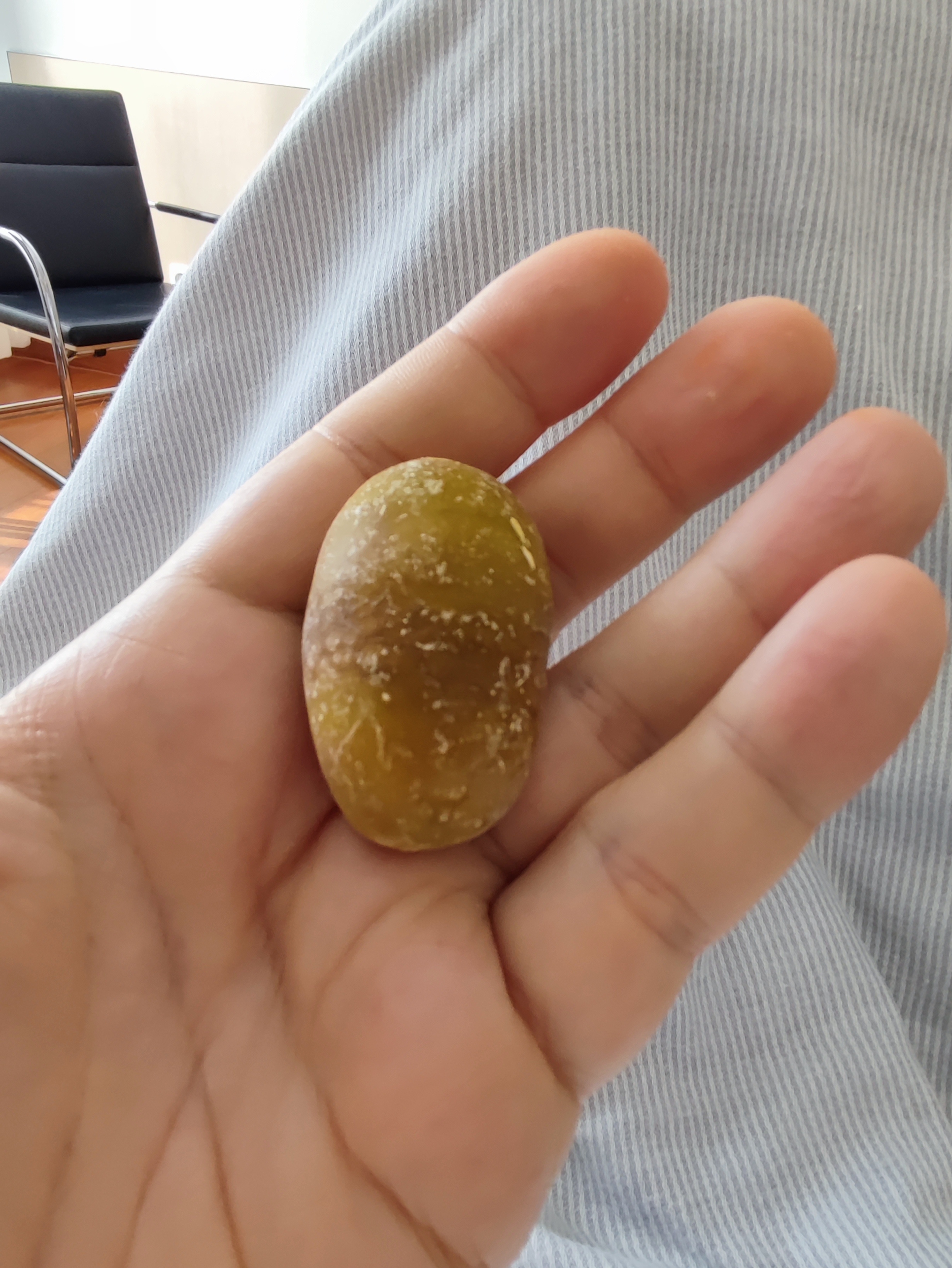 A hand holding a small, oval object with a rough texture, possibly a seed or stone, against a fabric background