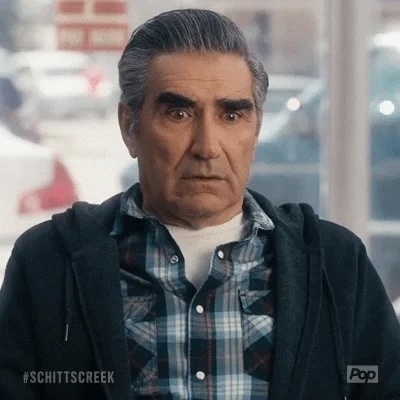 Eugene Levy, with a serious expression, wears a plaid shirt and a jacket in a scene from the TV show "Schitt's Creek."