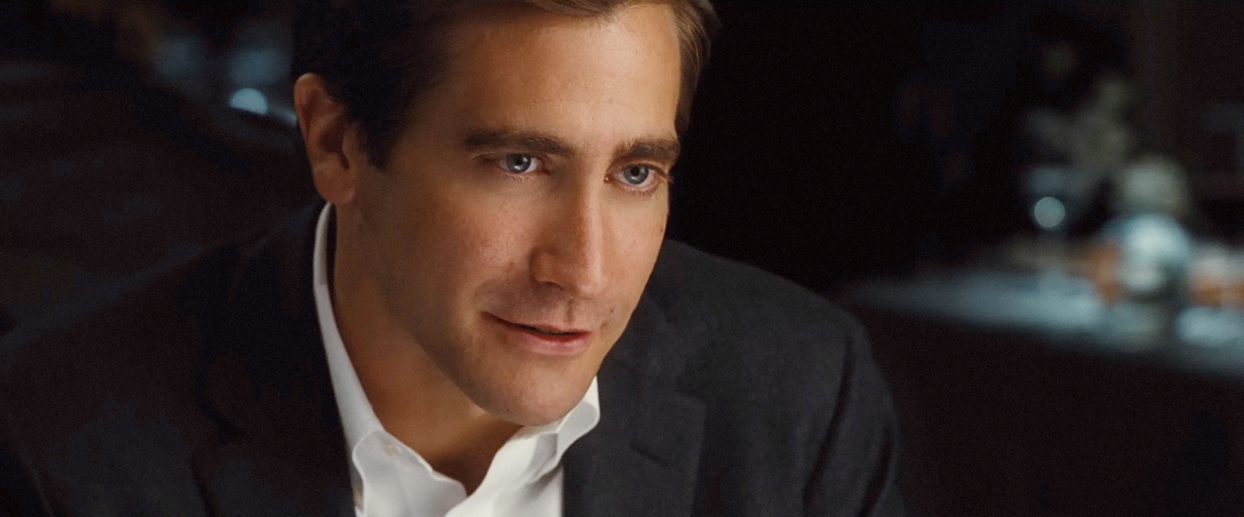 Jake Gyllenhaal in conversation, wearing a suit jacket over a white shirt, from a scene in a movie