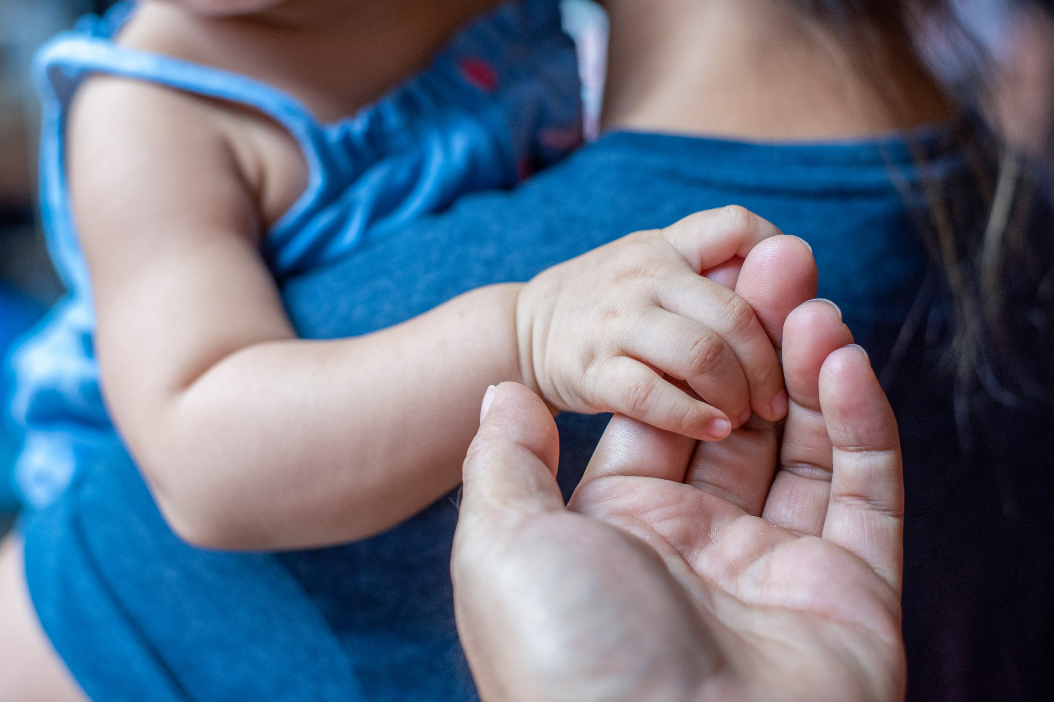 A baby gently holds an adult's hand while being carried by another person