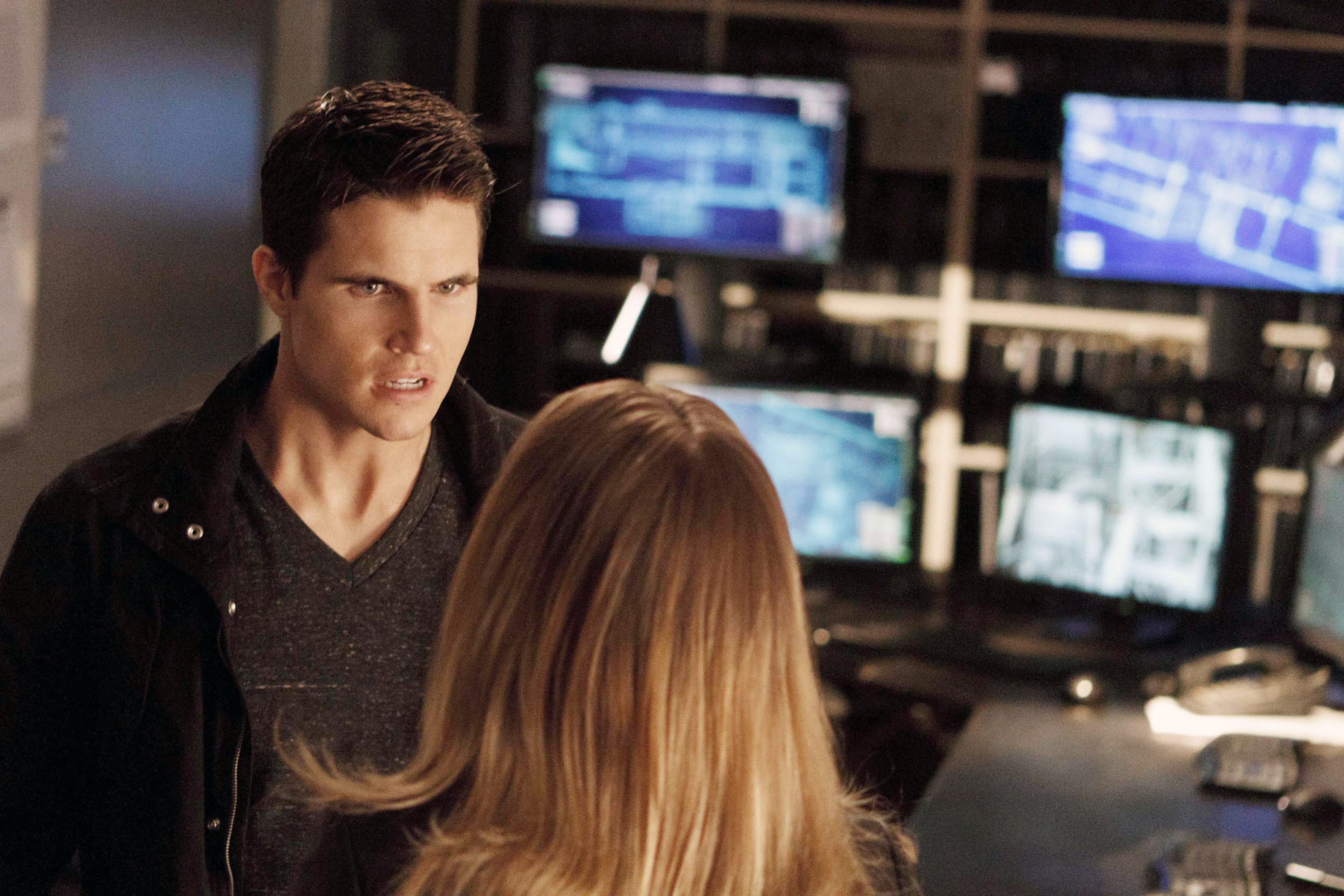 Stephen Amell and Robbie Amell in an intense conversation, surrounded by computer monitors in a tech-filled room