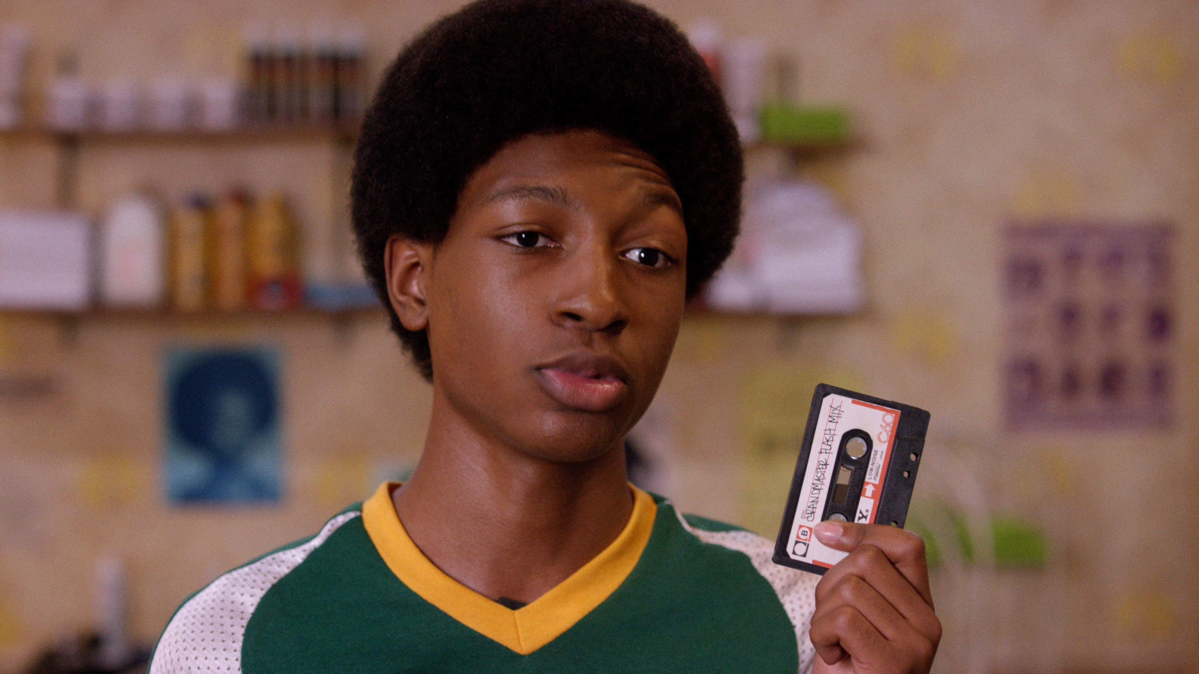 Person holding a cassette tape, wearing a sports jersey in a scene from a TV show or movie