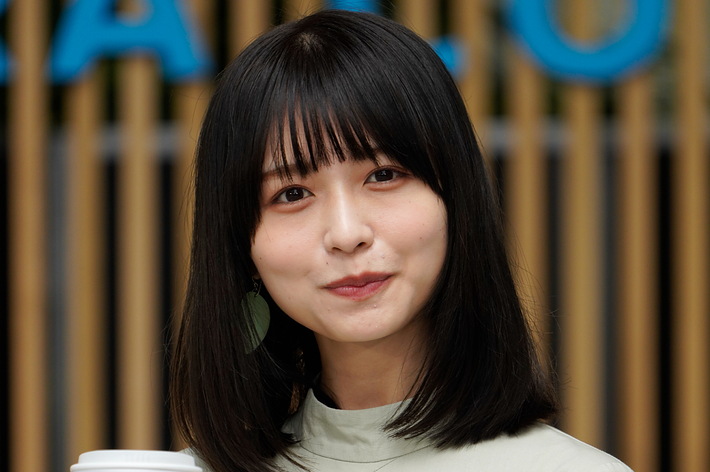 女性がカフェのロゴが入ったカップを持ち、カメラに向かって微笑んでいる。