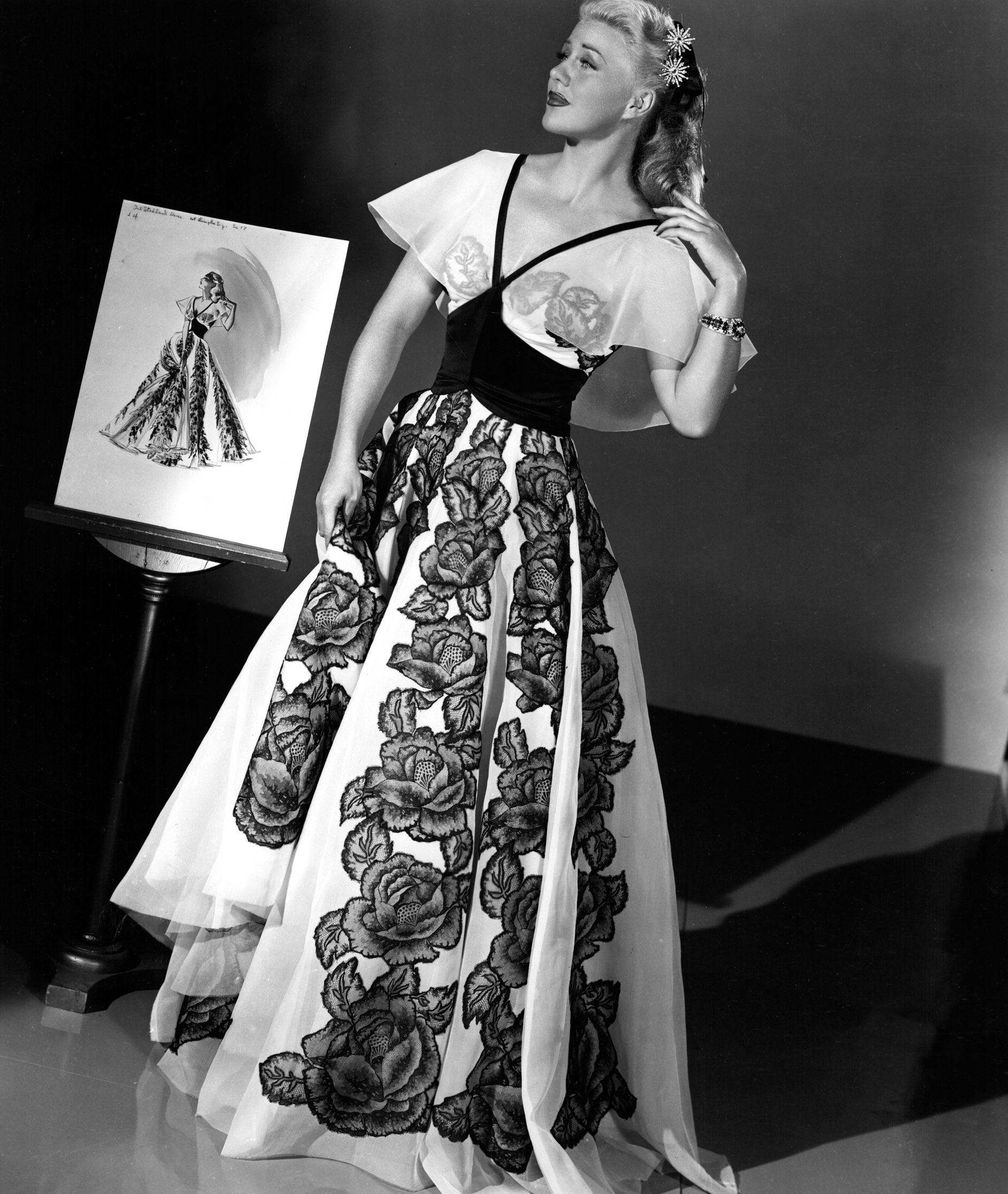 Ginger Rogers wearing an elegant gown with floral patterns, standing beside a portrait of herself in the same dress