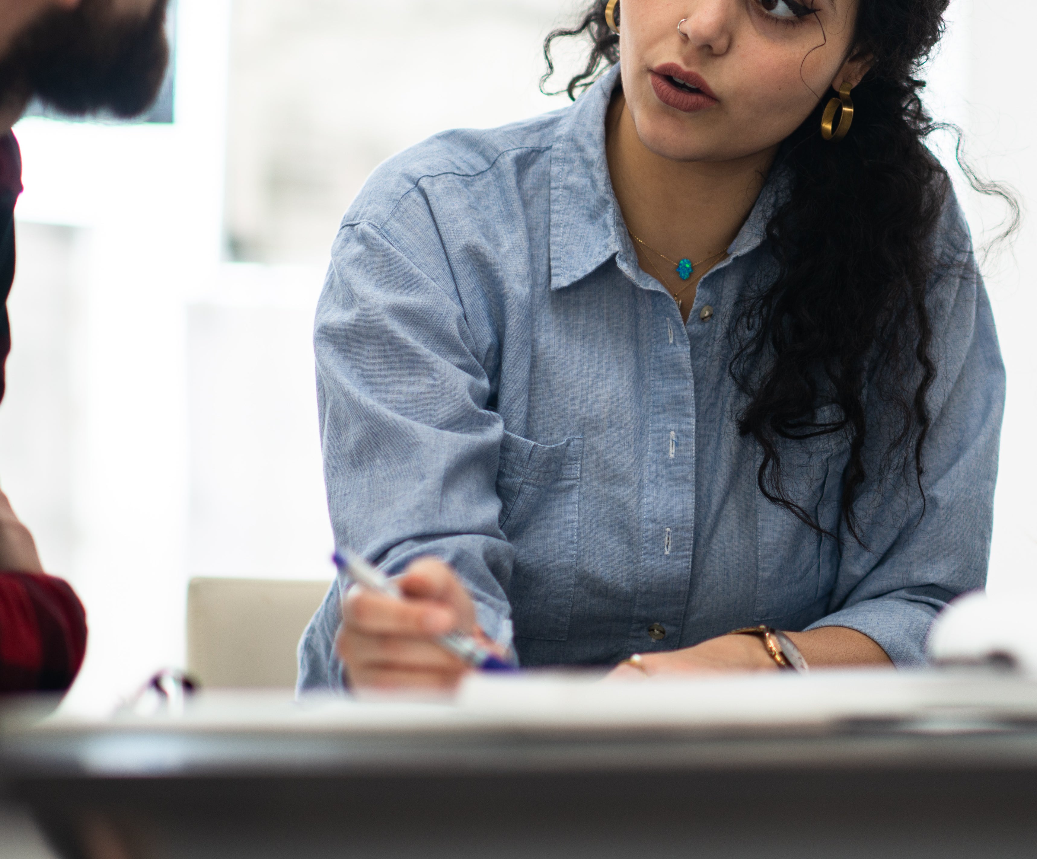 Two people engaged in a serious conversation at a table. The woman is holding a pen and paper.