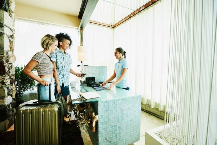 Two people check into a hotel, smiling and handing over documents at the reception desk. A receptionist assists them