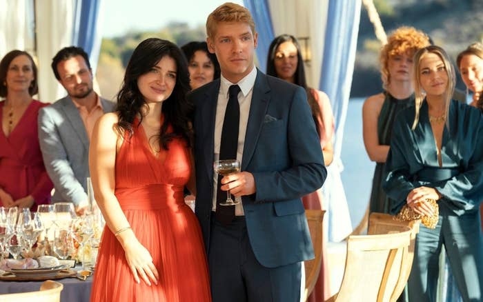 Phoebe Dynevor, vestida con un vestido de gala, y un hombre con traje y corbata en un evento elegante, rodeados de otros invitados