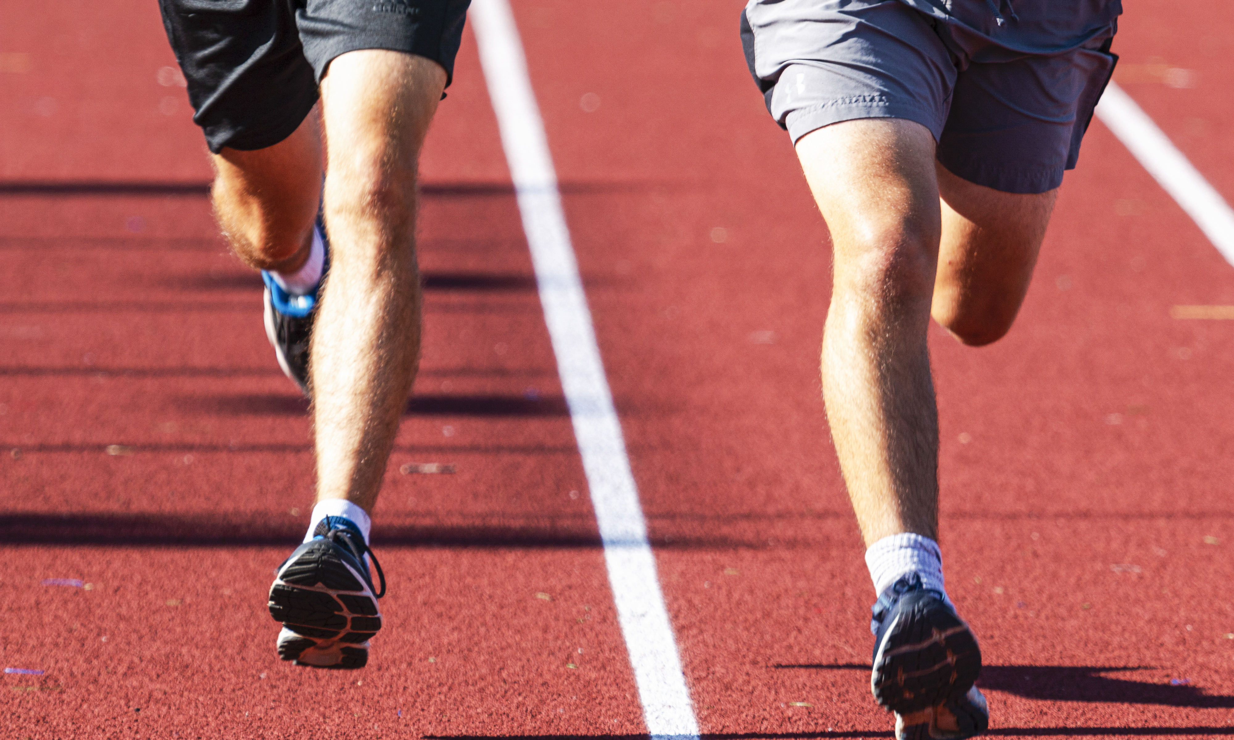 Two people running on a track, with only their legs and shoes visible