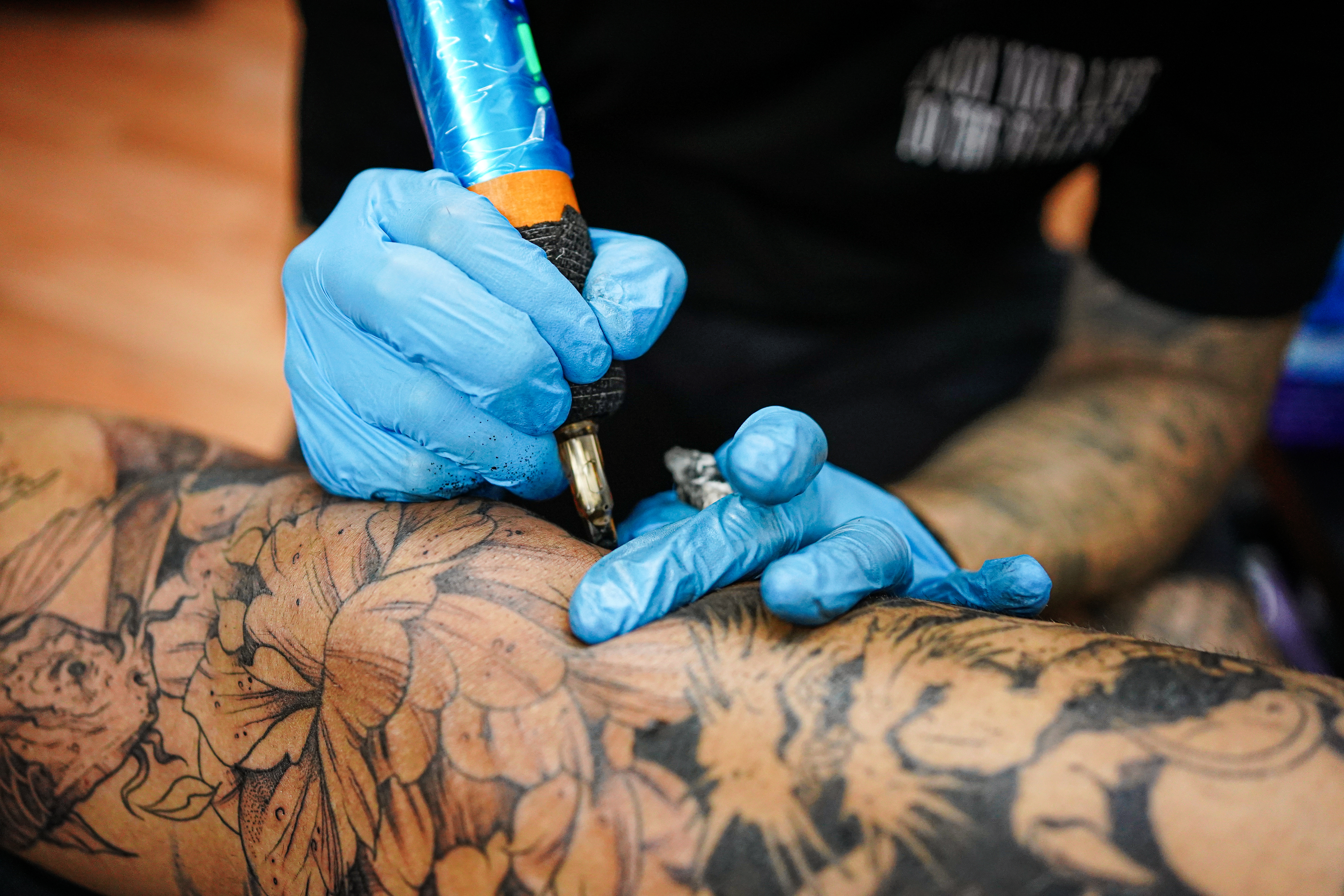 Close-up of a tattoo artist's gloved hands as they tattoo a person's with a black and gray floral design