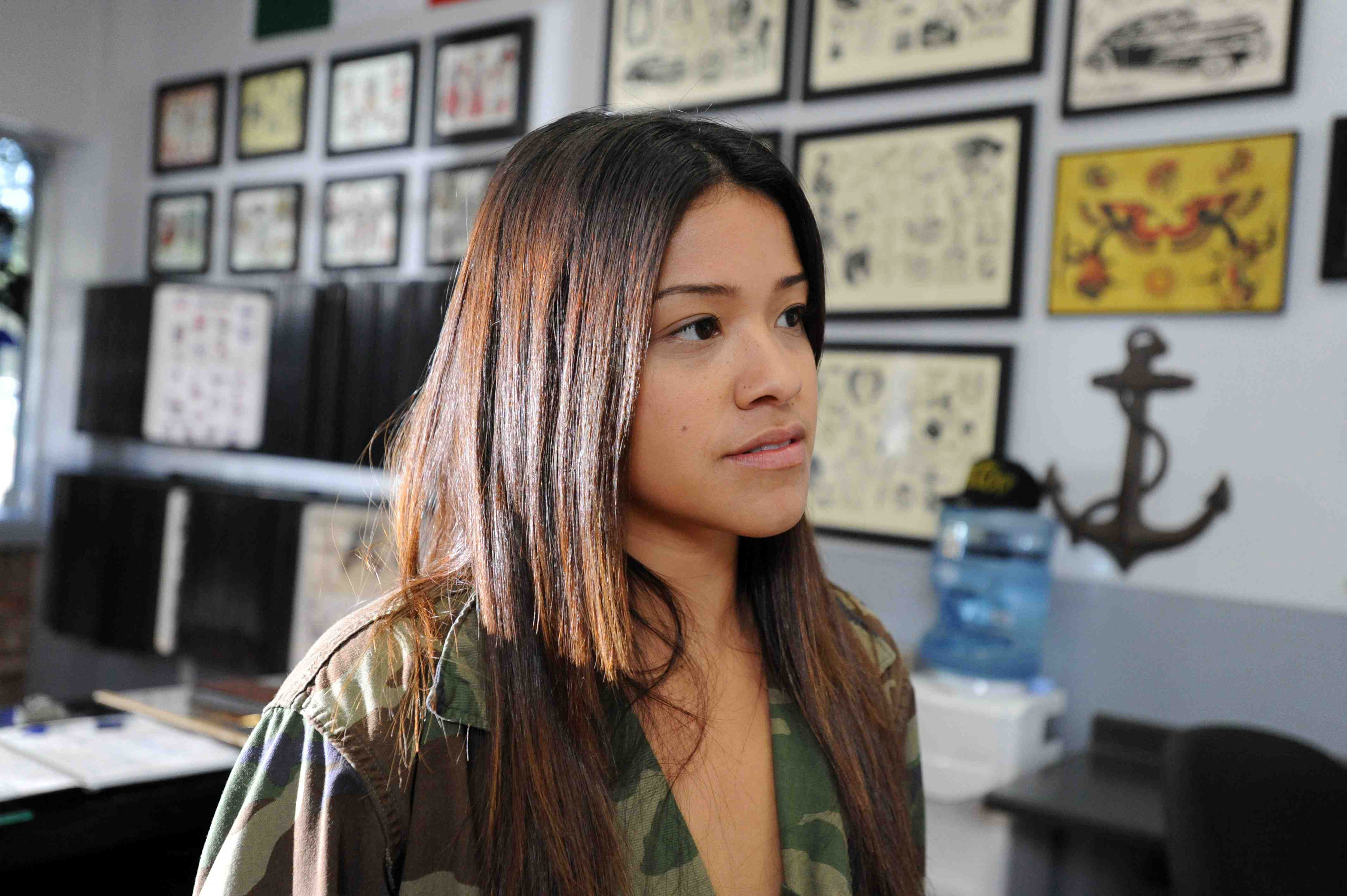 Gina Rodriguez standing in a tattoo shop with flash pieces in frames on the wall in "Filly Brown"