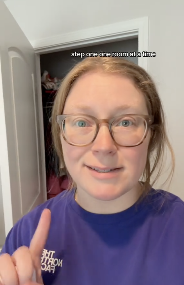 Cindell stands in front of an open closet holding one finger up.