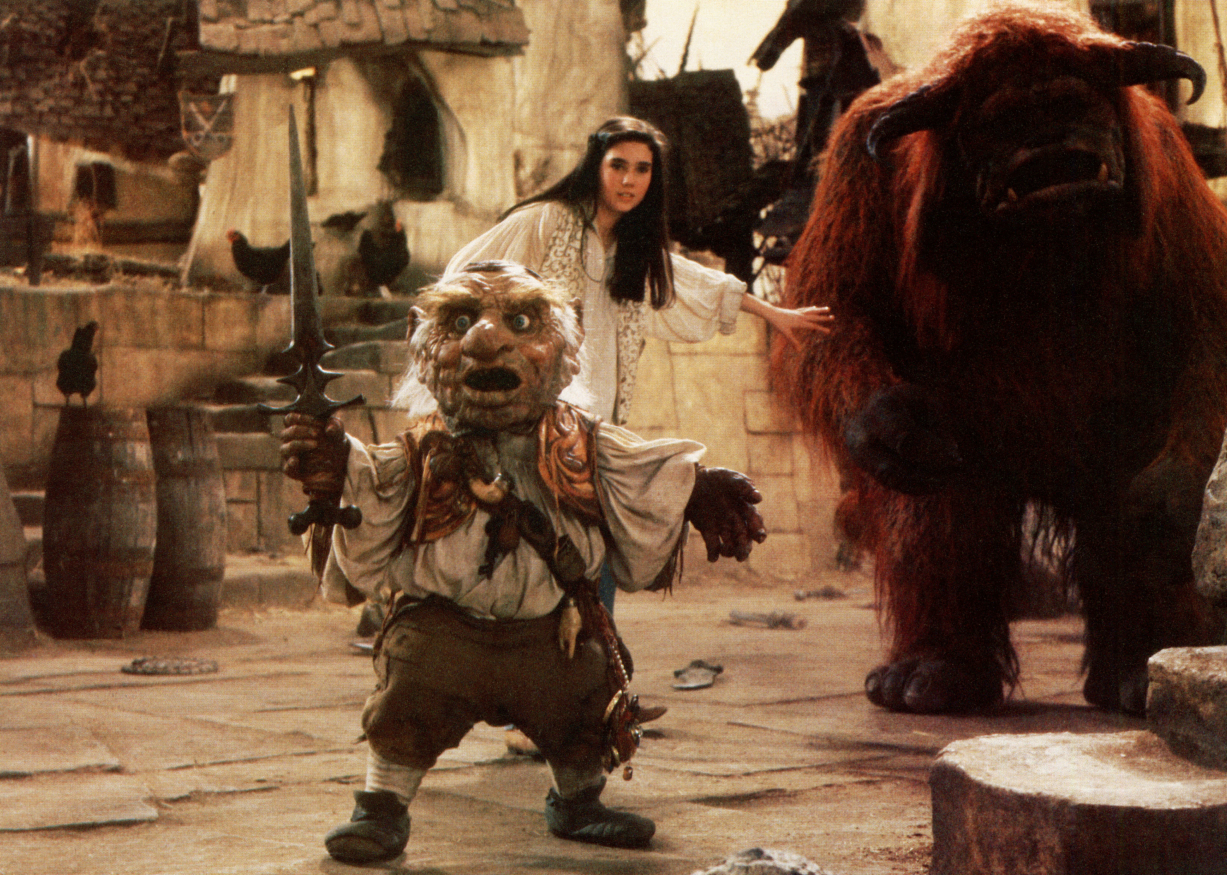 Jennifer Connelly, costumed as Sarah, stands near Hoggle and Ludo in a castle courtyard scene from the film "Labyrinth."
