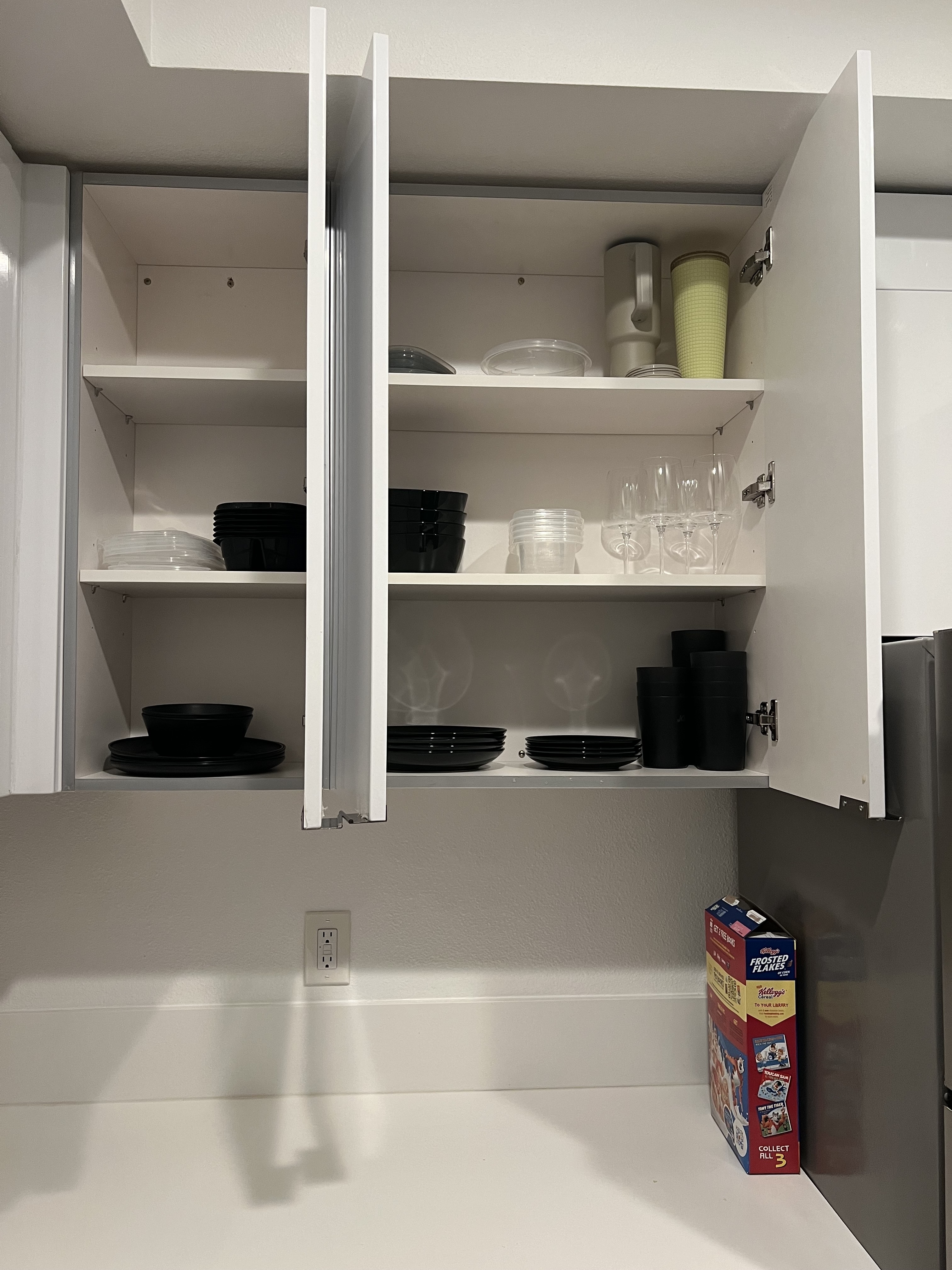 Open kitchen cabinet with neatly organized black and white dinnerware, cups, and stacked plates and bowls