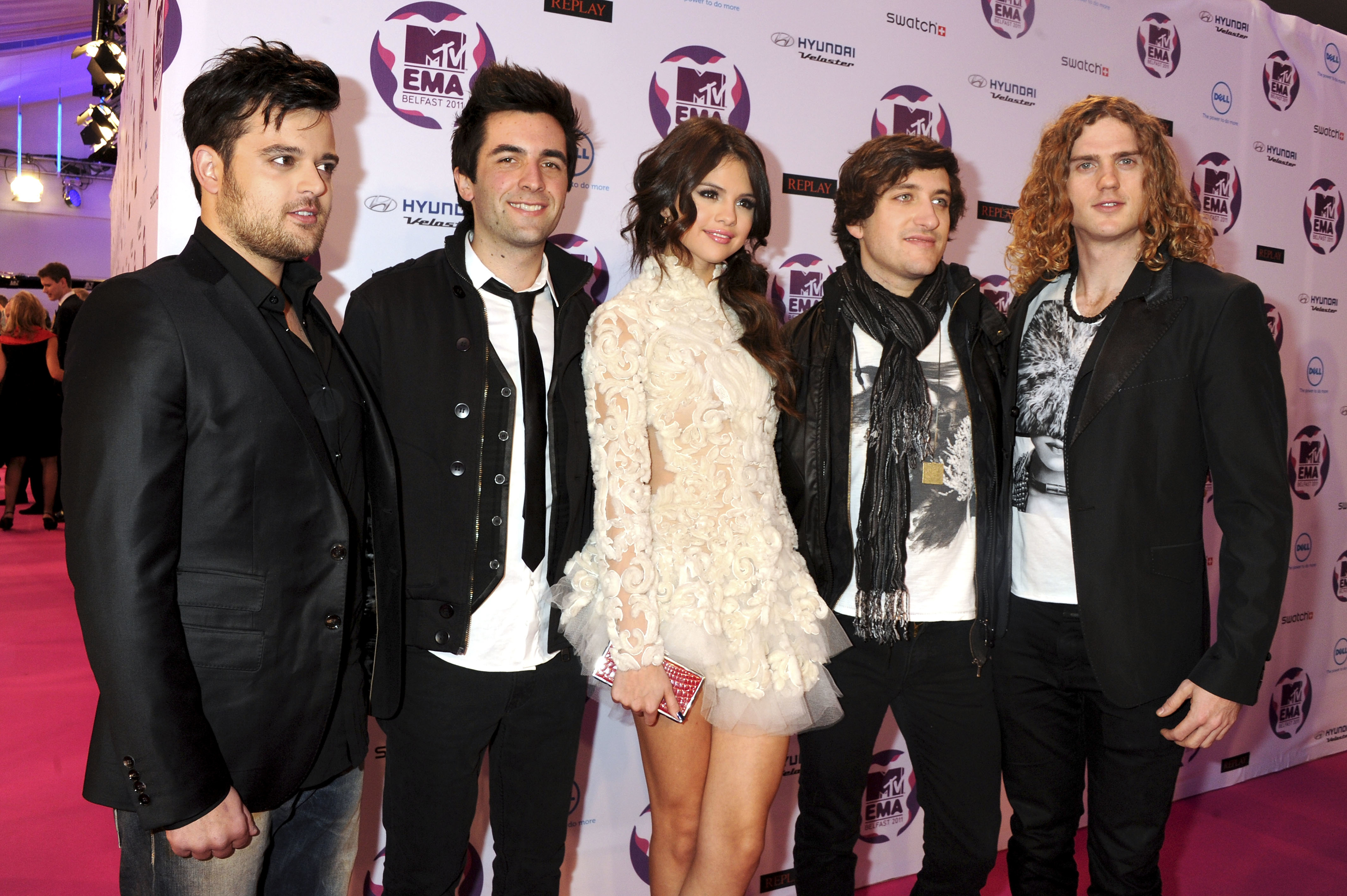 A group photo on the red carpet of the MTV EMAs featuring Selena Gomez in a white ruffled dress with four men from the band, The Scene