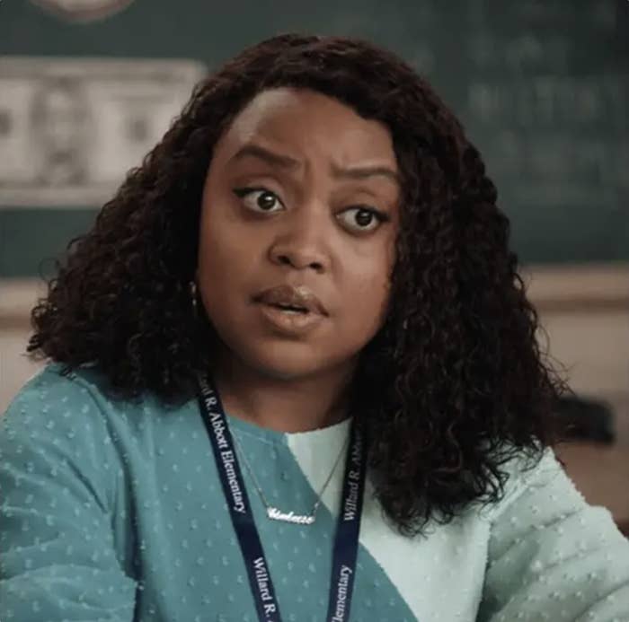 Quinta Brunson is captured expressing a serious look while seated in a classroom, wearing a lanyard and a blue sweater