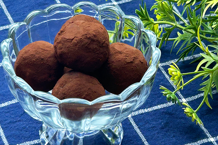 ガラスの器に盛られたチョコレートトリュフがテーブルに置かれている。隣には緑の観葉植物。
