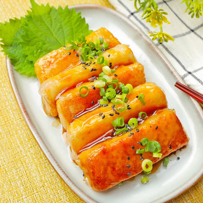 お皿に盛り付けられたタレをかけた焼き料理。ネギとごまがトッピングされている。