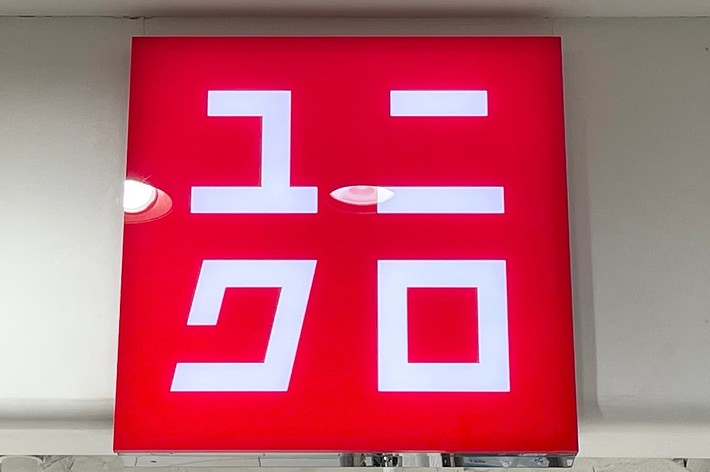 Red and white Uniqlo store sign with Japanese characters, mounted on a white ceiling with visible air ducts
