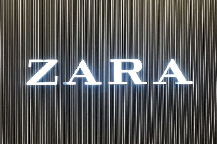 The image shows the Zara store sign with illuminated letters against a vertically striped background