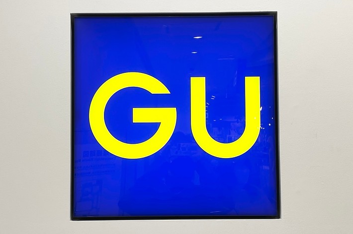 A square sign with the letters &ldquo;GU&rdquo; prominently displayed in yellow. The background is blue