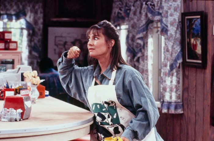 Bonnie Bramlett as Bonnie Watkins in a kitchen scene from the TV show &quot;Roseanne,&quot; wearing a denim shirt and a cow-themed apron, holding a cleaning cloth