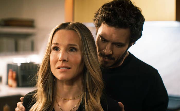 Kristen Bell and Adam Brody in a kitchen scene, with Adam standing closely behind Kristen, who looks concerned