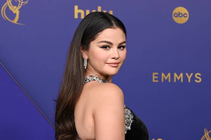 Selena Gomez on the Emmys red carpet, wearing a sleeveless dress with embellishments and large, sparkling earrings, posing with a slight smile
