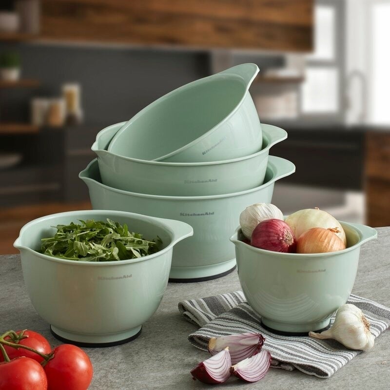 Three bare  stacked mixing bowls connected  a room  antagonistic  with a smaller mixing vessel  with onions and different  tiny  mixing vessel  with arugula