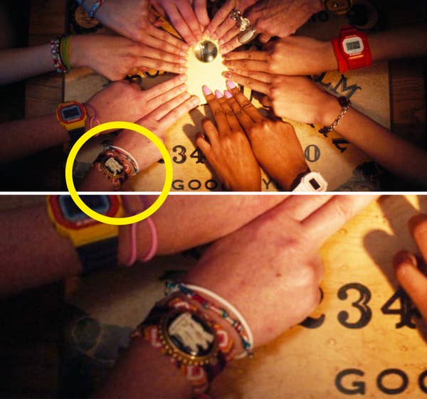 Hands gathered around an Ouija board with fingers on the planchette, various watches and bracelets visible