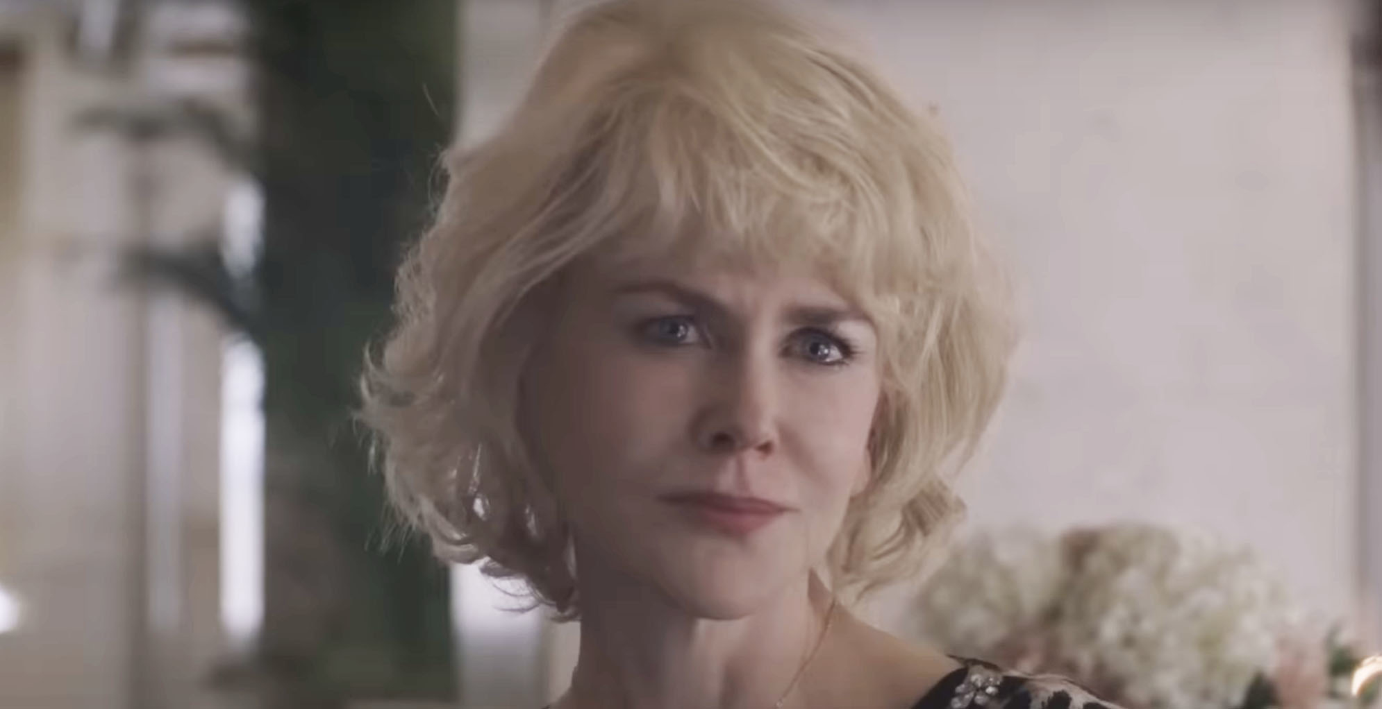 I don’t know who this is, but it shows a woman with short, wavy hair, wearing a patterned top, looking directly at the camera in a setting with blurred foliage