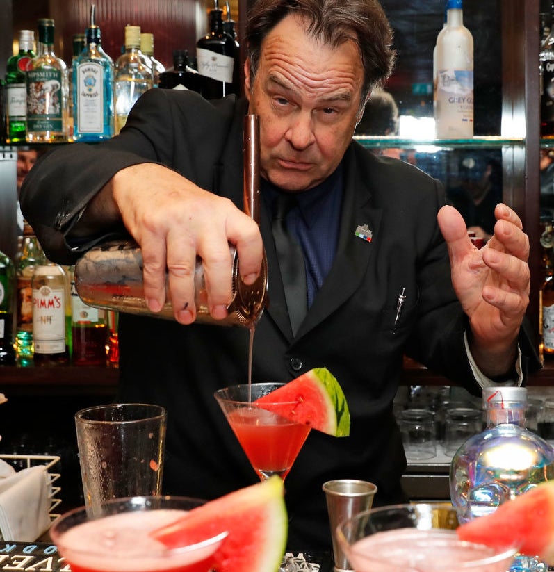 A bartender pours a cocktail at a bar, surrounded by various bottles