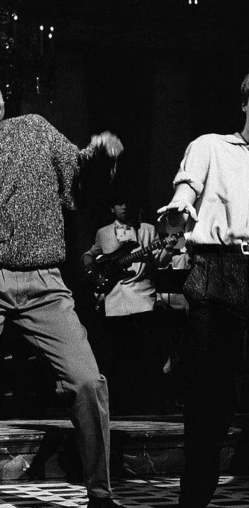 Two people dancing energetically at a club. They are wearing stylish casual outfits suitable for the lively atmosphere