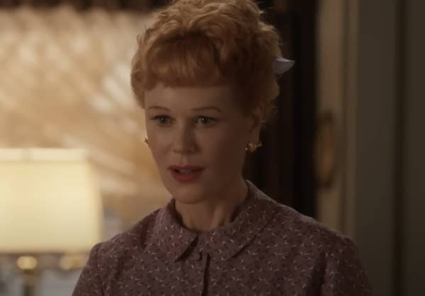 A woman in vintage clothing with short, curled hair is standing indoors