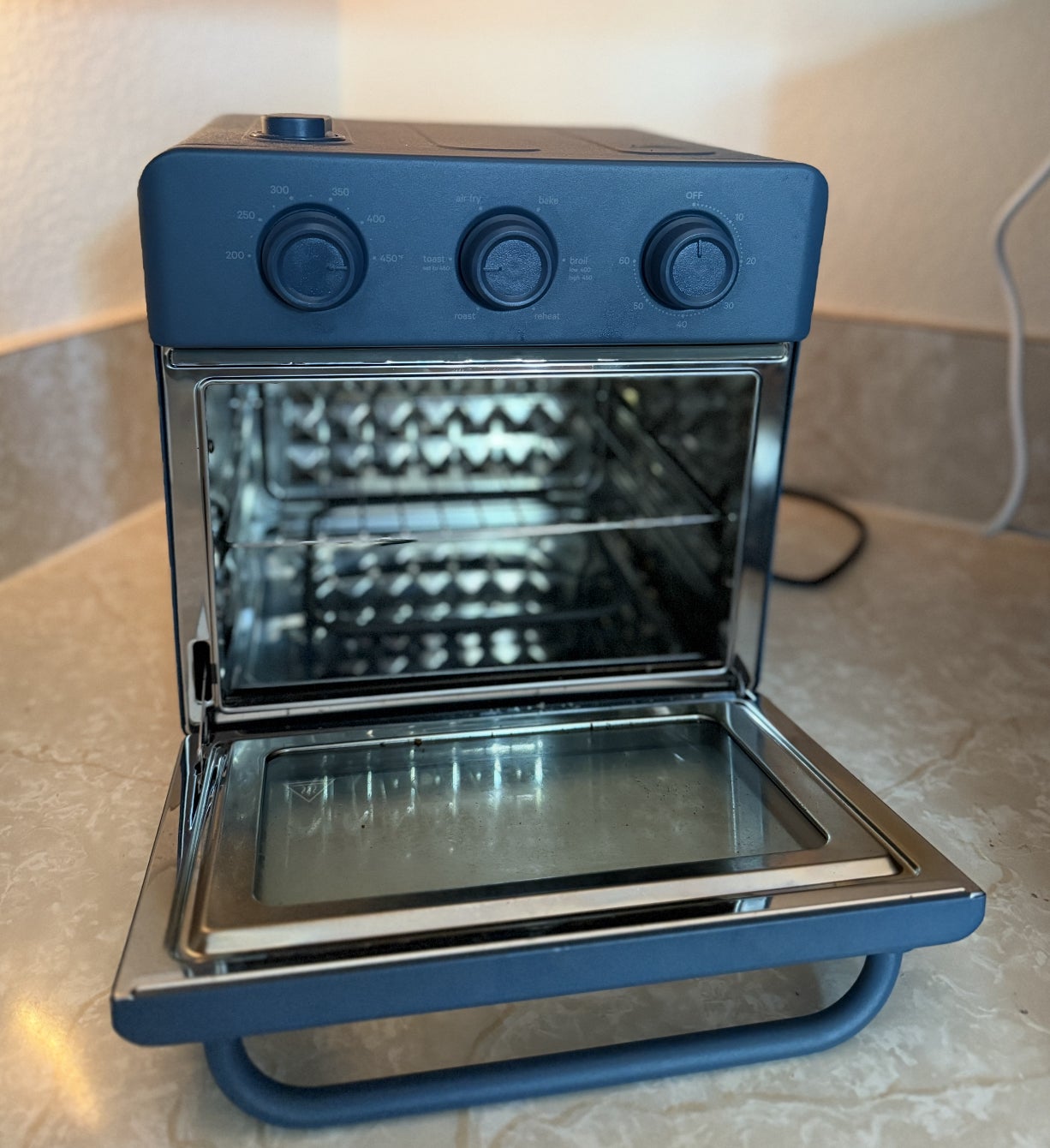 Electric toaster oven with open door, stainless steel interior, and dial controls on a kitchen countertop
